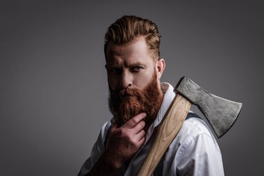 Sakallı adam, baltayı tut. Saç ve sakal bakımı. Yakışıklı, sakallı, vahşi adam. Sakal şekillendirme. Bıyıklı, Kafkas bir hippi. Sakallı adam gri yolda izole edilmiş. Klasik berber dükkanı..