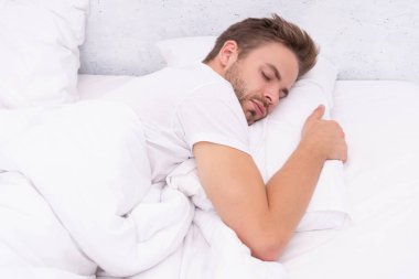 Genç adam uyuyor ya da beyaz yatak odasında evinde uyuyor..