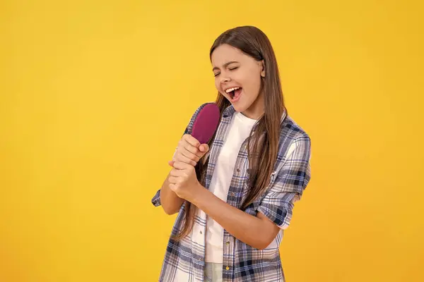 stock image positive teen girl doing haircare in studio. haircare of teen girl with hairbrush. teen girl taking care of her hair with a hairbrush, haircare. teen girl haircare by combing hair isolated on yellow.