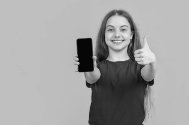 Sarı arka planda akıllı telefonu olan mutlu bir çocuk. başparmak yukarı.