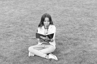 thinking teen child making notes in notebook sitting on grass. taking notes. student make notes outdoor.