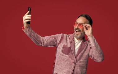 Şaşırmış selfie adamın telefon blogu. Selfie Adam 'ın telefonda blog yazarken çekilmiş fotoğrafı. Kırmızı arka planda izole edilmiş bir telefon blogunda şık bir adam. Adam stüdyoda telefon blogları için selfie çekiyor..