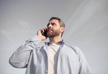 Sinyal iyi. Telefonda erkek erkeğe konuşma. Adam akıllı telefondan konuşuyor. Gökyüzü arka planında insan iletişimi.