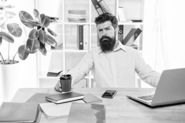 Tired guy drinking takeaway coffee working at office desk, coffee break.