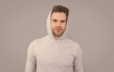 Erkek portresi. Yakışıklı adam sıradan bir kapüşonlu giyiyor. Tıraşsız yüzlü genç bir adam. Beyazların stüdyosu gri arka planda izole edilmiş..