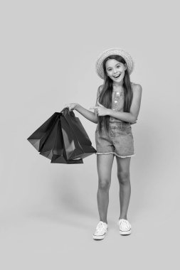 happy teen girl pointing finger on shopping bags on yellow background. full length.