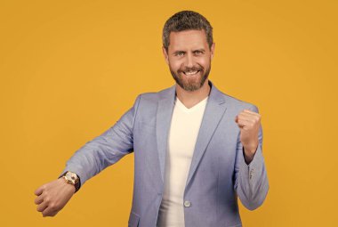 glad businessman follow punctuality with watch. businessman wearing watch. punctuality of businessman with watch in jacket isolated on yellow. businessman punctuality in studio. photo of handsome