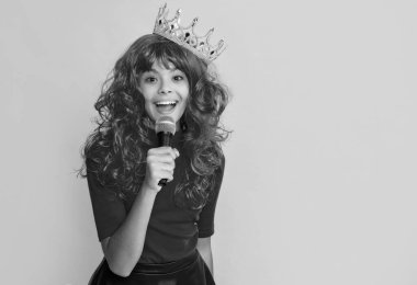 positive kid in crown with microphone on yellow background.