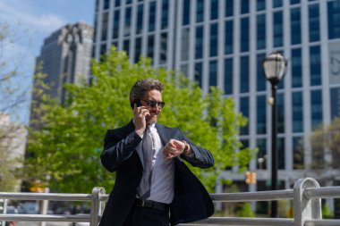 Takım elbiseli bir adam telefonda konuşuyor. Telefonu olan orta yaşlı İspanyol işadamı. İş iletişimi. İş adamının dışarıyı araması gerekiyor. İş adamı telefon kullanıyor ve saati kontrol ediyor.