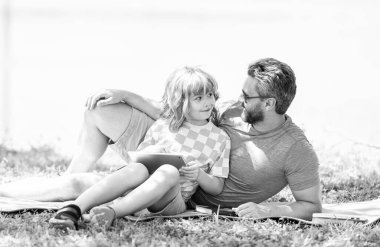 Baba oğul eğitimini tabletle şekillendirir. Baba ve oğul parkta dinleniyor. çocukluk okulu eğitimi. Oğlu ve babası yazın kaynaşıyorlar. Baba ve oğul eğitimi almış. Yeşil çimlerde rahatla.