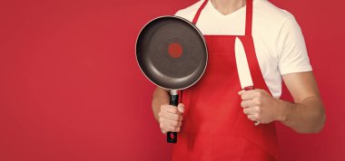 Kırmızı arka planda kızartma tavası ve bıçakla önlüklü neşeli olgun aşçı..