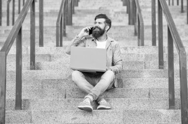 Cep telefonuyla konuşan mutlu adam dizüstü bilgisayarla çalışıyor. Gülümseyen adam dışarıda merdivenlerde otururken cep telefonuyla konuşuyor. Cep telefonundan arıyorlar. Mobil iletişim. Telefon görüşmesi.