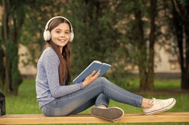 concept of teenage. Happy teenage girl reading and listening to audiobook in headphones after school outdoors, teenage.