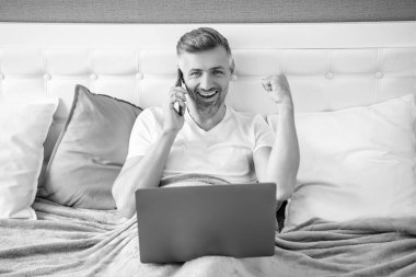 Başarılı bir yetişkin telefonda konuşuyor ve laptopla yatakta çalışıyor..