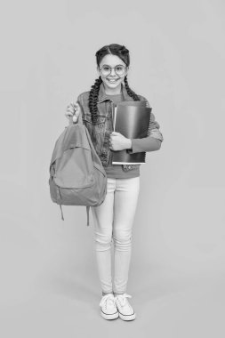 Okul çantasını sarı arka planda tutan mutlu genç kız. Okul eğitimi. Okula geri dön..