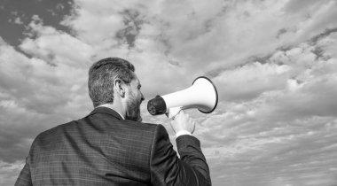 back view of businessman shout in loudspeaker on sky background. promotion.