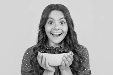 surprised teen girl hold cherry bowl on yellow background.