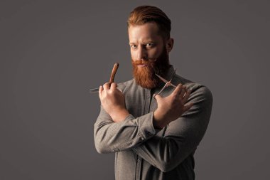 Berber dükkanındaki yakışıklı berber. Berber adam kuaförde makas ve bıçak tutuyor. Berber dükkanı konsepti. Berber adam gri arka planda izole edilmiş. Berber dükkanında elinde makas olan adam..