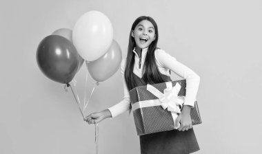 amazed child smile with party colorful balloons and present box on yellow background.