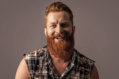 Sakallı, neşeli, vahşi, erkeksi bir adamın fotoğrafı. Gri renkte yalıtılmış vahşi, erkeksi bir adam. Stüdyodaki vahşi sakallı adam. Arka planda vahşi erkeksi erkek.