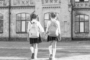 back view of two children with school backpack walking together outdoor.