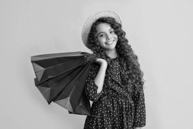 happy child with curly hair hold shopping bags on yellow background.