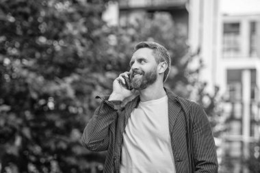 Sokakta akıllı telefon görüşmesi yapan mutlu bir adam. Adam dışarıdaki akıllı telefondan arıyor. Adamın fotoğrafı. Akıllı telefondan ara ve konuş. Adamın açık havada akıllı telefonu var..