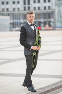 Smokinli zarif bir damat. Damat dışarıda smokin papyon takıyor. Gül ile yakışıklı damat.