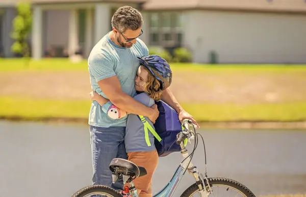 stock image father hugging son on bicycle at fathers day. father setting a example for fathers son. fathers parenting with son outdoor. childhood of son supported by fathers care. Creating memories.