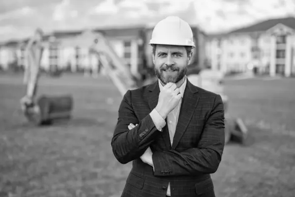 stock image photo of positive civil engineering supervisor wearing hardhat. civil engineering supervisor in suit. civil engineering supervisor at site. civil engineering supervisor outdoor.