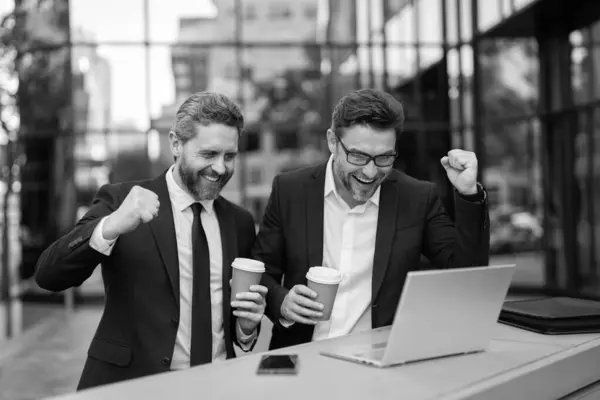 Stock image two happy trader men freelancing online outdoor with laptop.