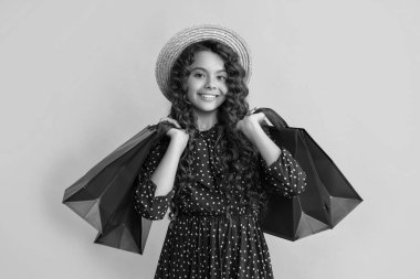 Kıvırcık saçlı mutlu kız sarı arka planda alışveriş torbaları tutuyor..