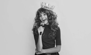 girl smile in crown with microphone on yellow background.