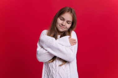 Sıcak kışlık kıyafetler giyen genç bir çocuğun portresi. Kız çocuğu kırmızı üzerine kalın bir kazak giyer. Mutlu şık bir çocukluk dilerim. Kazaklı genç kız. Kış modası. Örgü elbiseli kız. Pist eğilimleri.