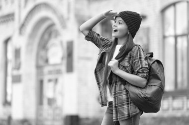 Happy teen girl back-to-school looking into distance keeping hand above eyes outdoors, copy space.