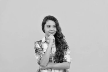 pondering teen child in checkered shirt with long curly hair on yellow background.