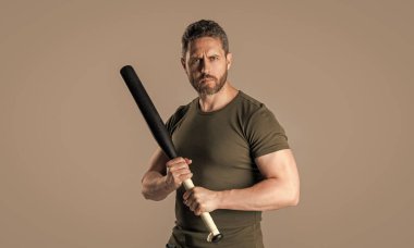 Stüdyoda beyzbol sopası olan kaslı bir suçlu. Sopalı suçlu adamın fotoğrafı. Yarasayla tehdit eden bir suçlu. Gri arka planda yarasalı bir suçlu var..