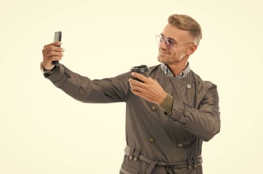 Mutlu gülümseyen iş adamı iş adamı işadamı patronu resmi palto giymiş iş telefonuyla selfie çekiyor. Kahve fincanı stüdyosu beyaz, selfie 'de izole edilmiş..