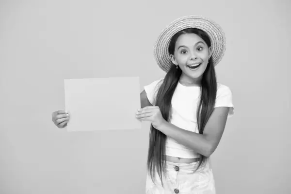 stock image amazed teen girl hold empty advertisement paper with copy space on yellow background.