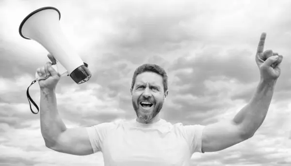 stock image man in yellow shirt shout with loudspeaker on sky background.