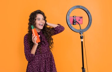 cheerful kid with long curly hair making video for blog hold shampoo.