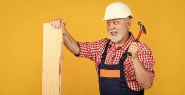 happy aged man woodworker in helmet on yellow background.