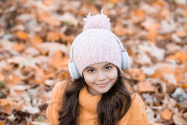 Parkta, sonbaharda, şapkalı neşeli çocuk kulaklıkla müzik dinliyor..