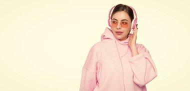 Ciddi kız öğrenci, günlük pembe kapüşonlu ve gözlüklü. İnternetten öğreniyor. Kulaklıklarda ses kurslarını dinliyor..
