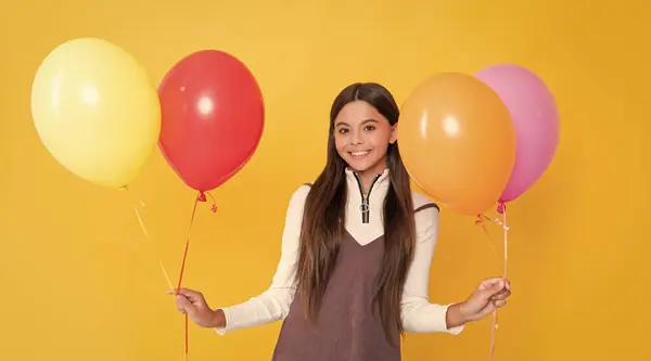 Stock image positive child with party colorful balloons on yellow background.