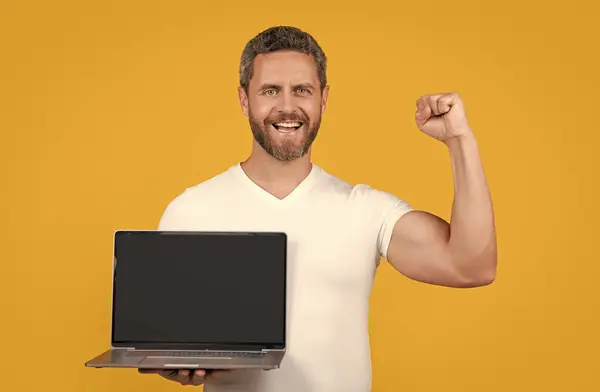 stock image happy man showing laptop app in studio. man showing app on laptop. man showing app on screen with copy space. man showing app isolated on yellow background.