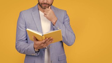 İnsan okuyucunun kitap okurken çekilmiş bir fotoğrafı. Adam okuyucu kitabı sarı arka planda izole edilmiş. Adam okuyucu ceketinde kitap okuyor. İnsan okuyucunun kitap okurken çekilen bir fotoğrafı..
