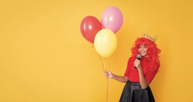 Sarı arka planda mikrofonlu ve parti balonlu pozitif çocuk..