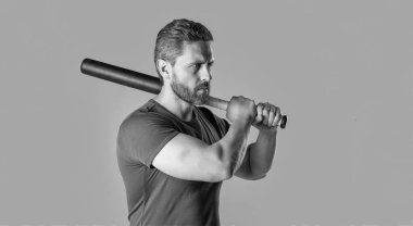 Kızgın adamın saldırganlığı stüdyoda sopayla dövüldü. Sopayı tutan kızgın adamın fotoğrafı. Kızgın adam tehdit ediyor. Öfkeli adam öfkesini gri arka planda yalnız yarasayla ifade eder.