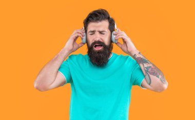 Sakallı adam sarı arka planda izole edilmiş kulaklıkla müzik dinliyor. Adam kulaklıkla müzik dinliyor. Müzik konseptini dinle. Kulaklıklı adamın stüdyo fotoğrafı. Havalı adam müzik dinler..